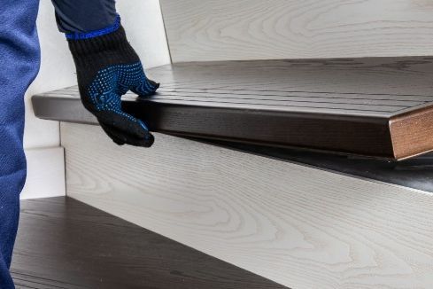 Person montiert Holzstufe auf Treppe